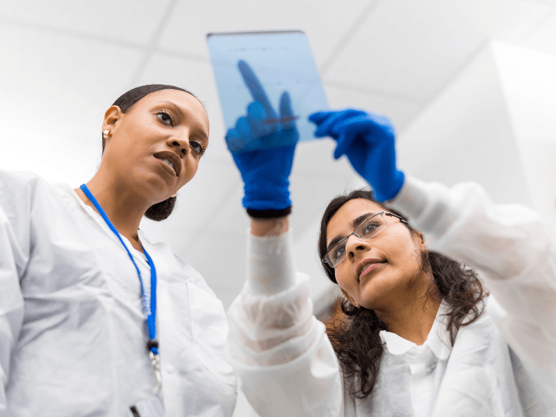 two women in science lab looking at up at a clip board