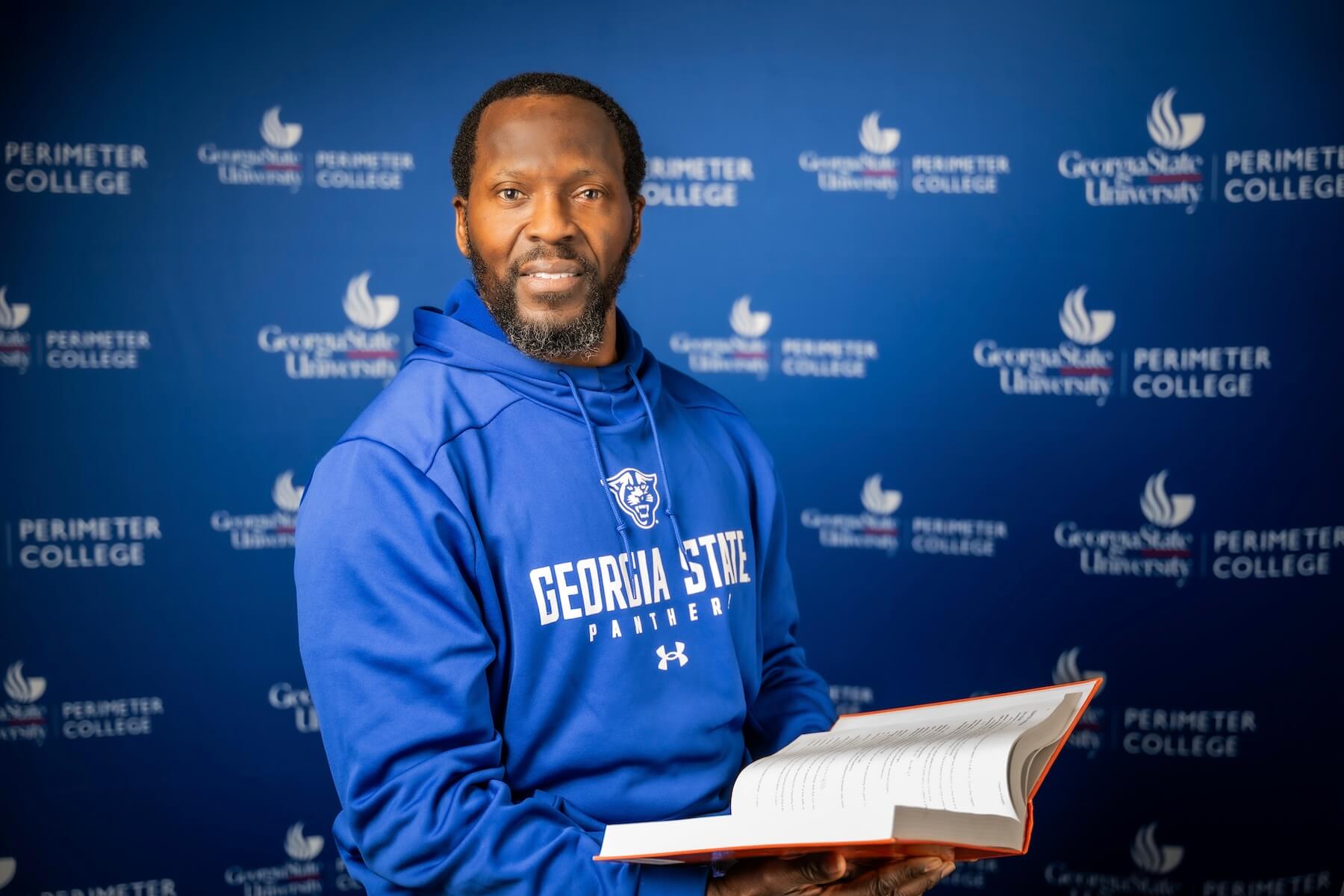 Student in blue hoodie holds an open book.
