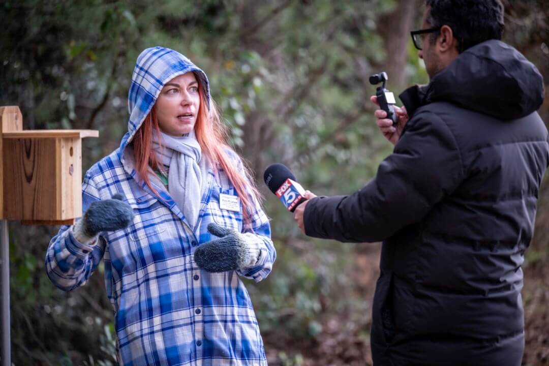 Woman in winter coat is interviewed by a man with microphone.