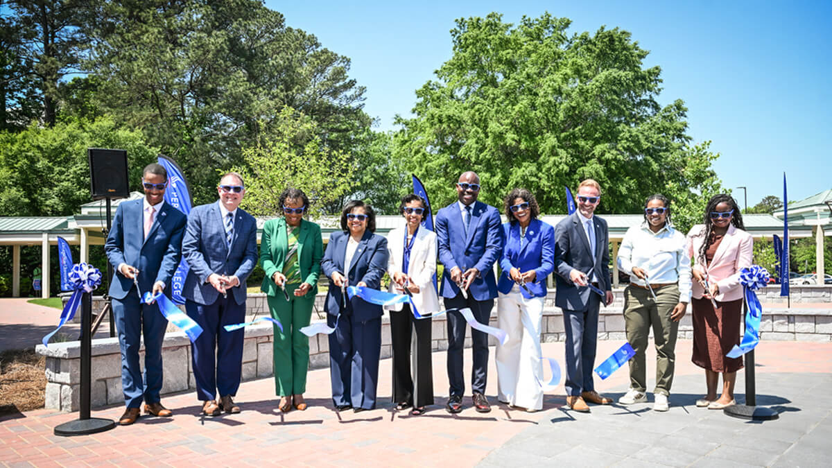 Ten people line up outdoors to cut a ribbon on the Panther Quad.