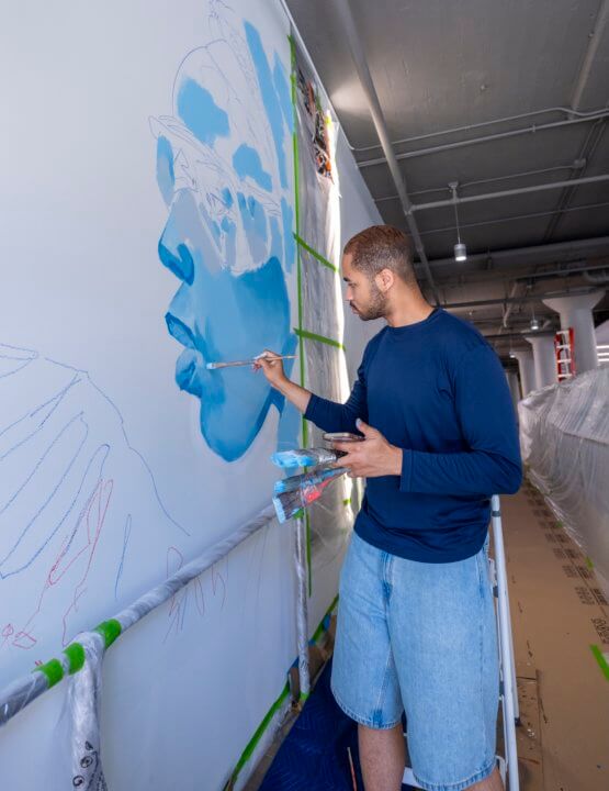 Demetri Burke paints a blue figure on a wall as part of his mural at the University Club at Edgewood.