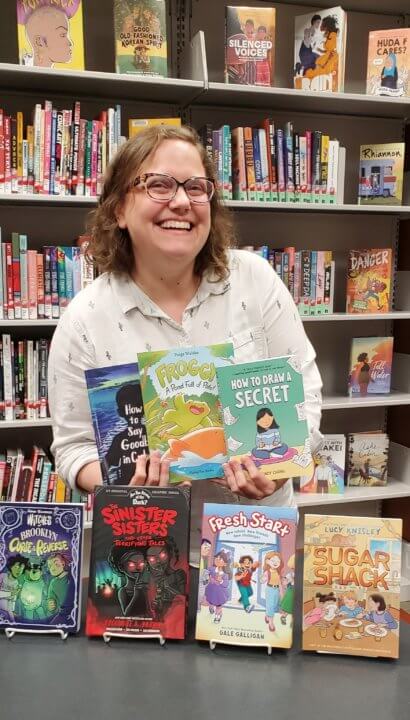 Woman wearing glasses holds graphic novels in a library