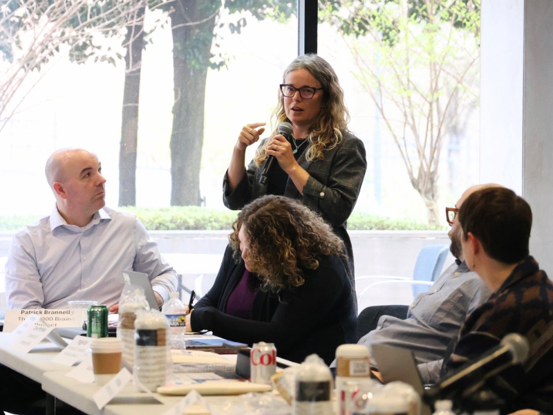 White woman standing speaking into a mic with onlookers
