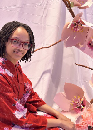 Harper poses beside a floral art installation featuring large pink blossoms and branching stems.