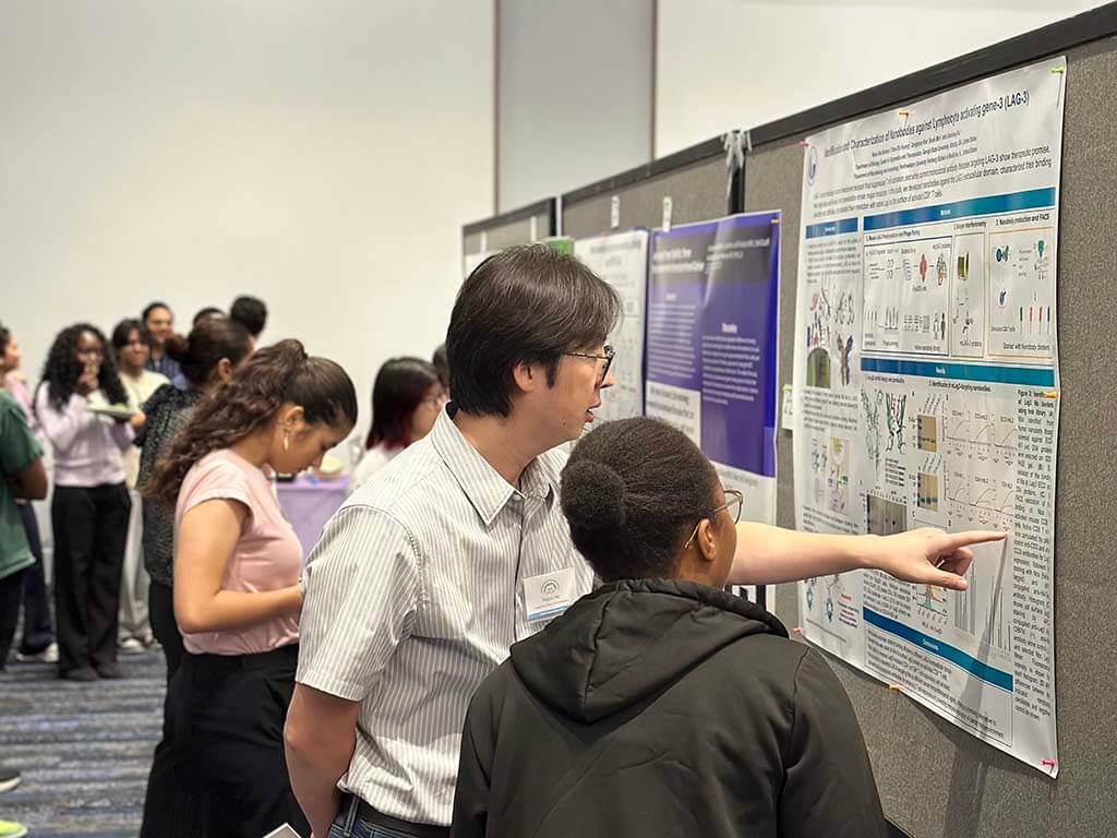 A faculty member and student discuss a research poster at IBMS Research Day 2026.