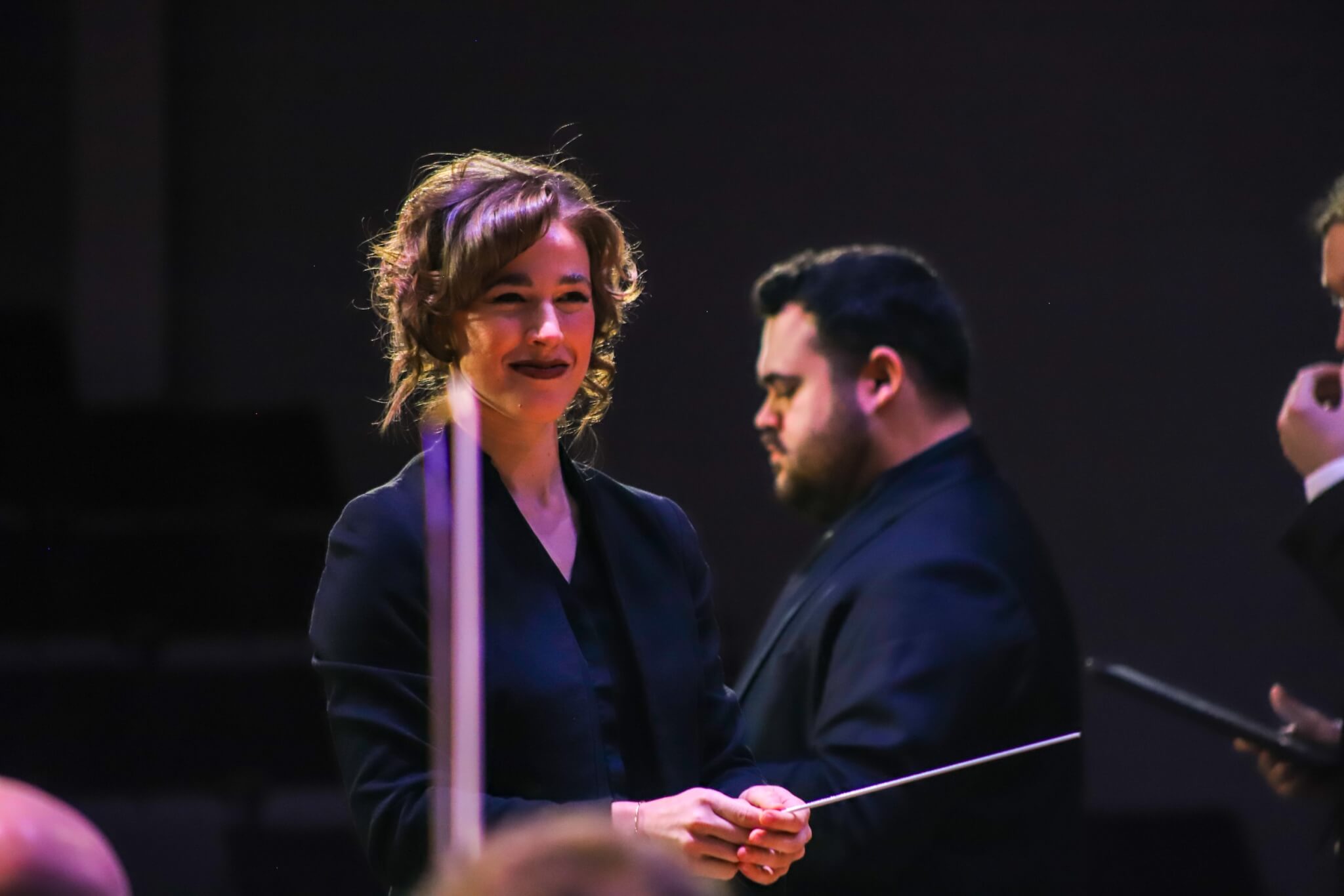 Woman with a baton conducting musicians.