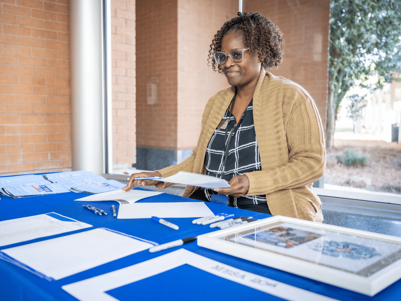 Woman in cardigan smiles while sitting at a registration table.