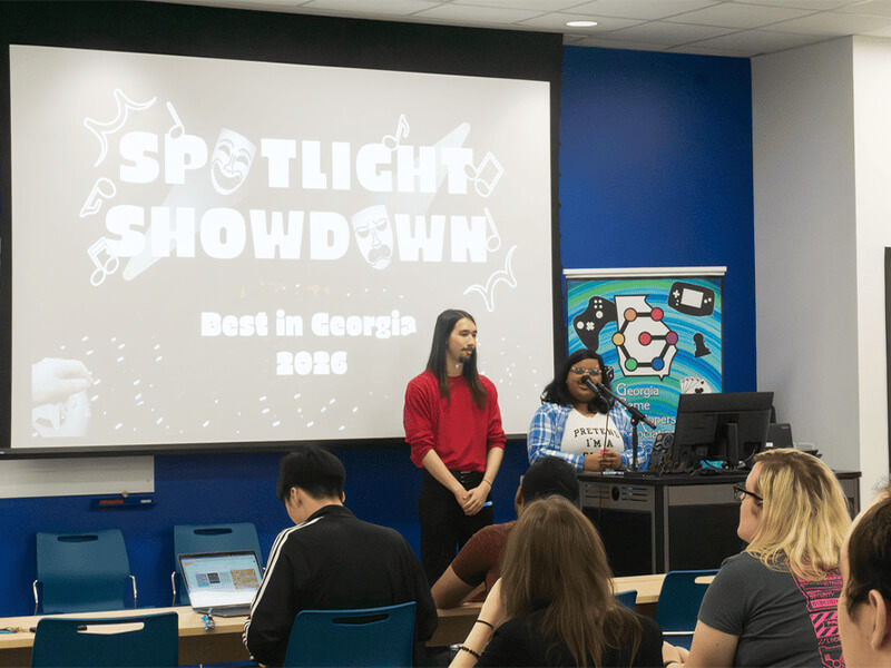 Students present the game "Spotlight Showdown" in front of a projector screen.