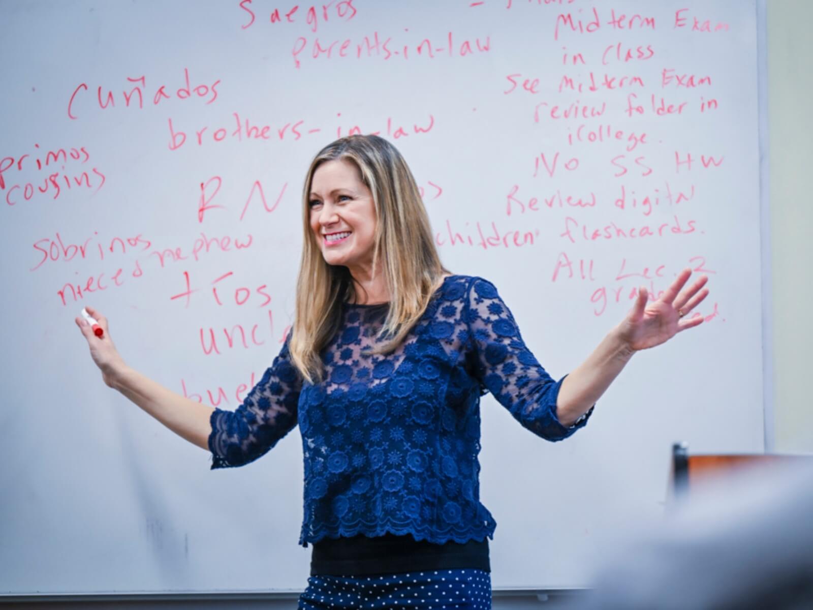 Professor stands in front of whiteboard in classroom.