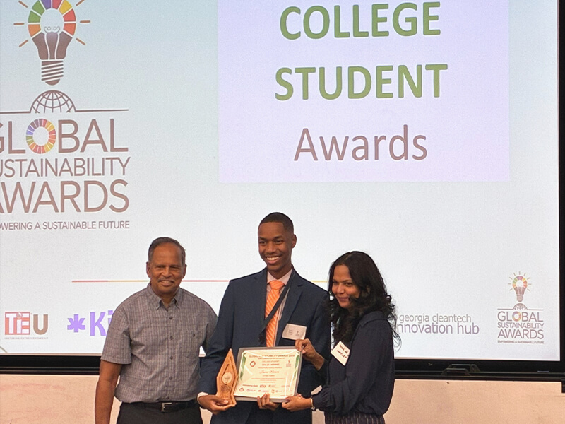 Three people posing in front of a screen, with the man in the middle holding a certificate.