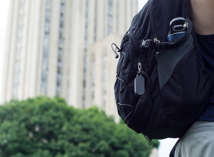 GoSafely keychain attached to a black backpack, with trees and a fuzzy building in the background