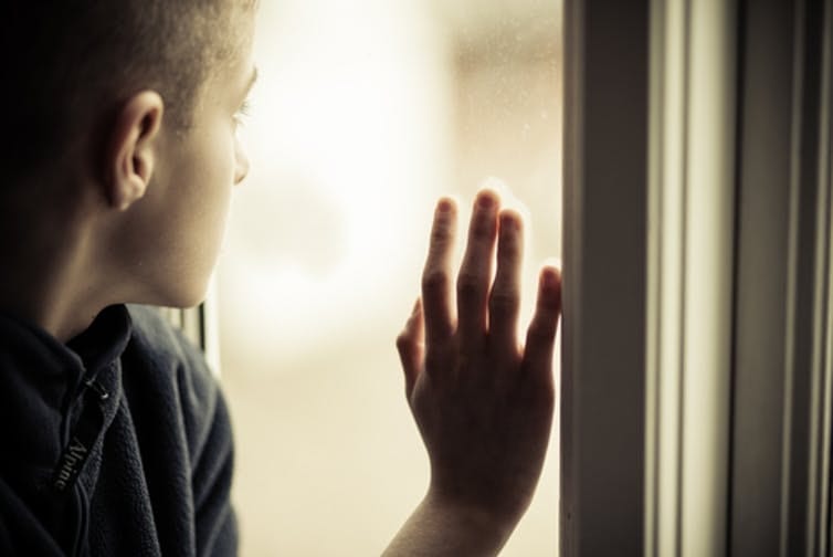 Young boy looks out a window with his hand upon the pane.