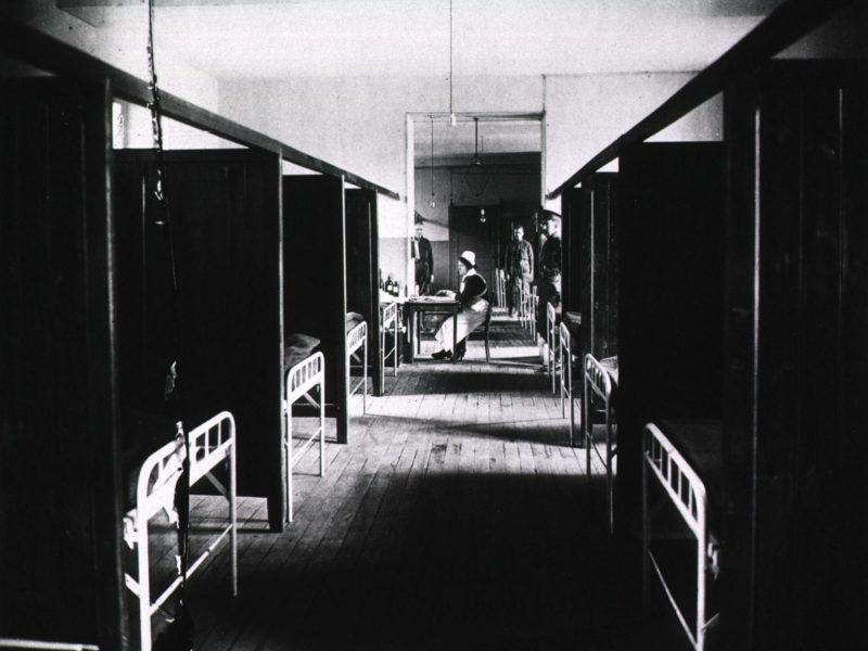 Vintage black and white photograph of a hospital floor with partitions and metal frame beds