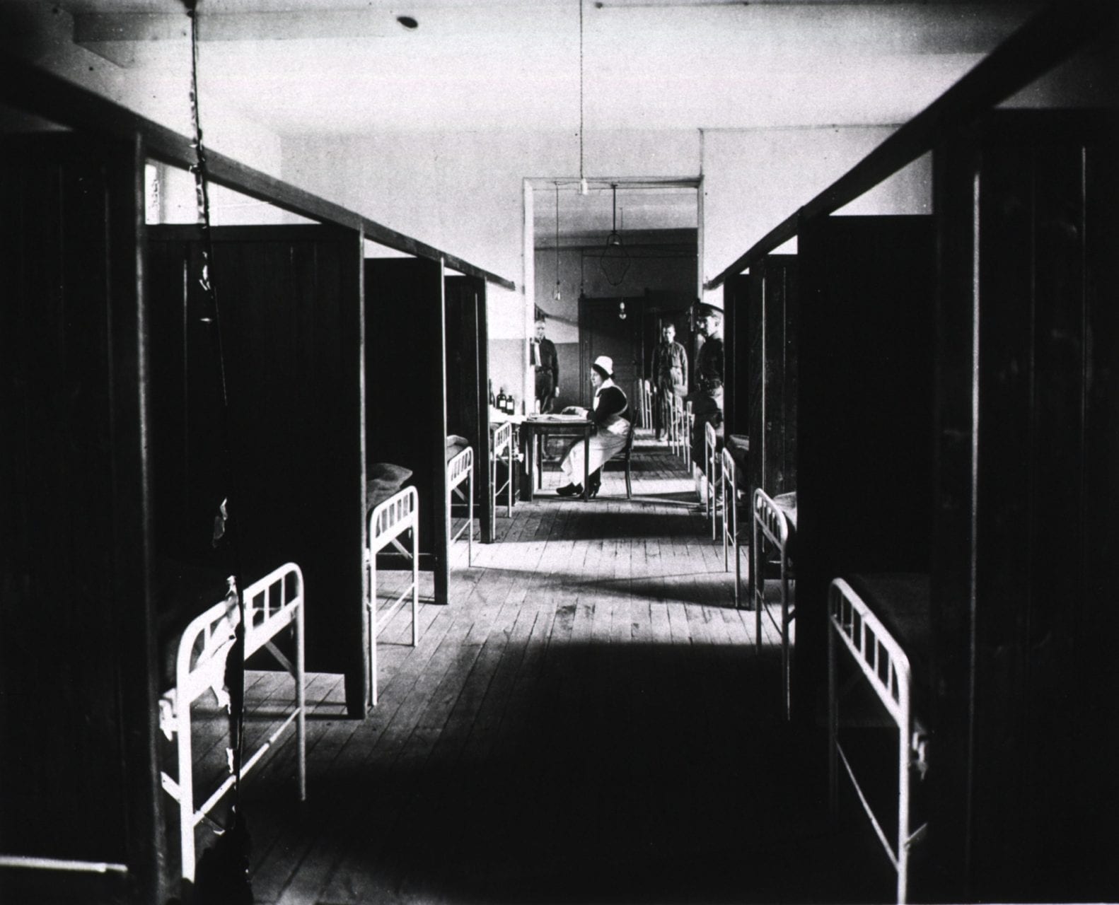 Vintage black and white photograph of a hospital floor with partitions and metal frame beds