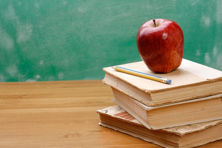 apple and a pencil sitting on a stack of books in a classroom