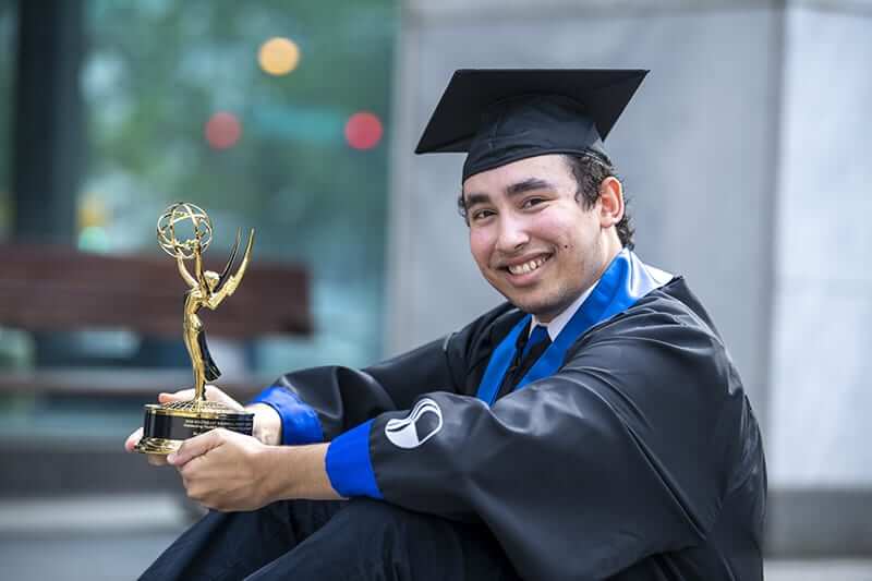 Georgia State student Riuki Gaiko wearing his cap and gown holding his Emmy Award.