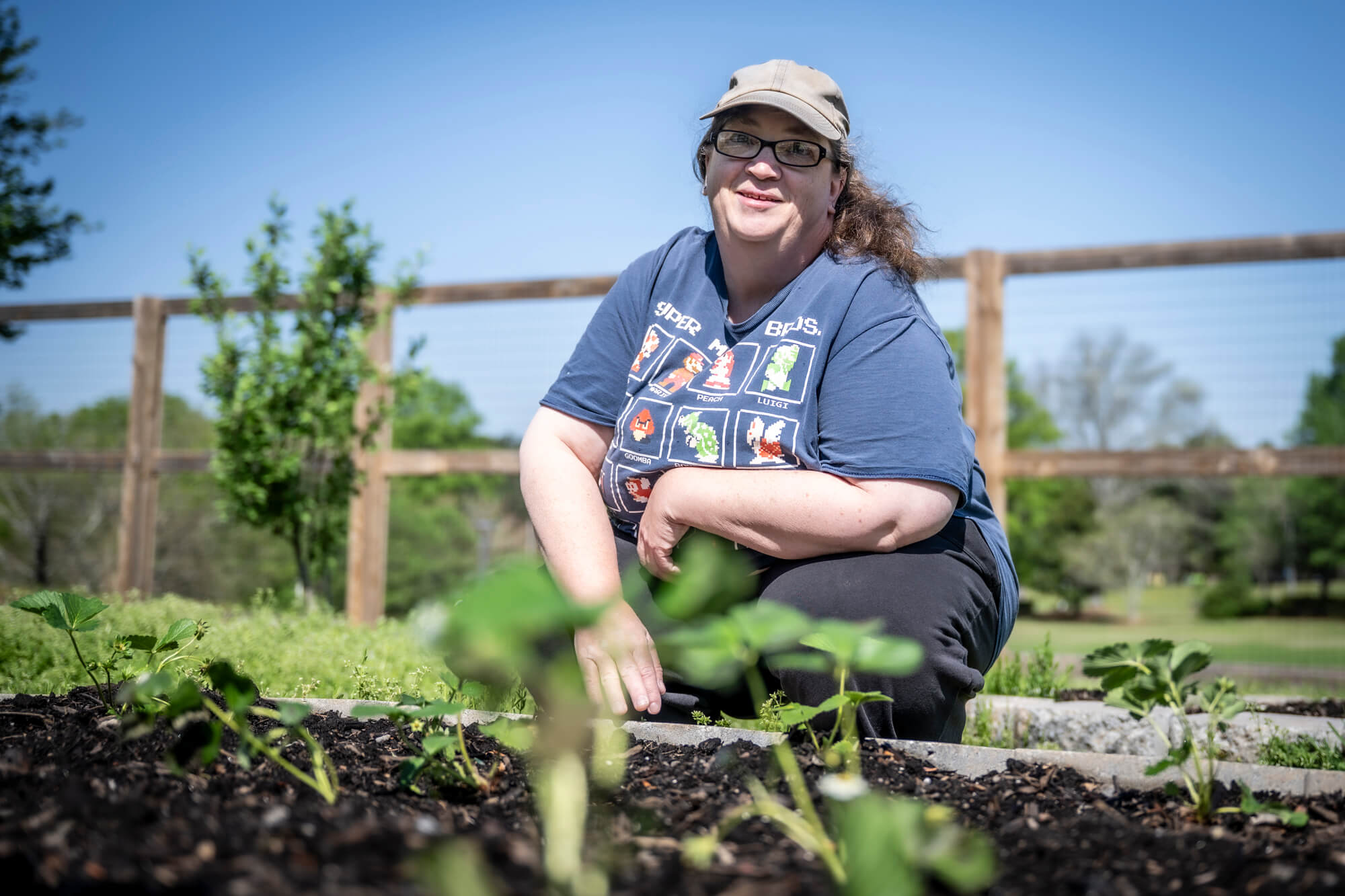 Woman in ball cap smiles while working in a garden.