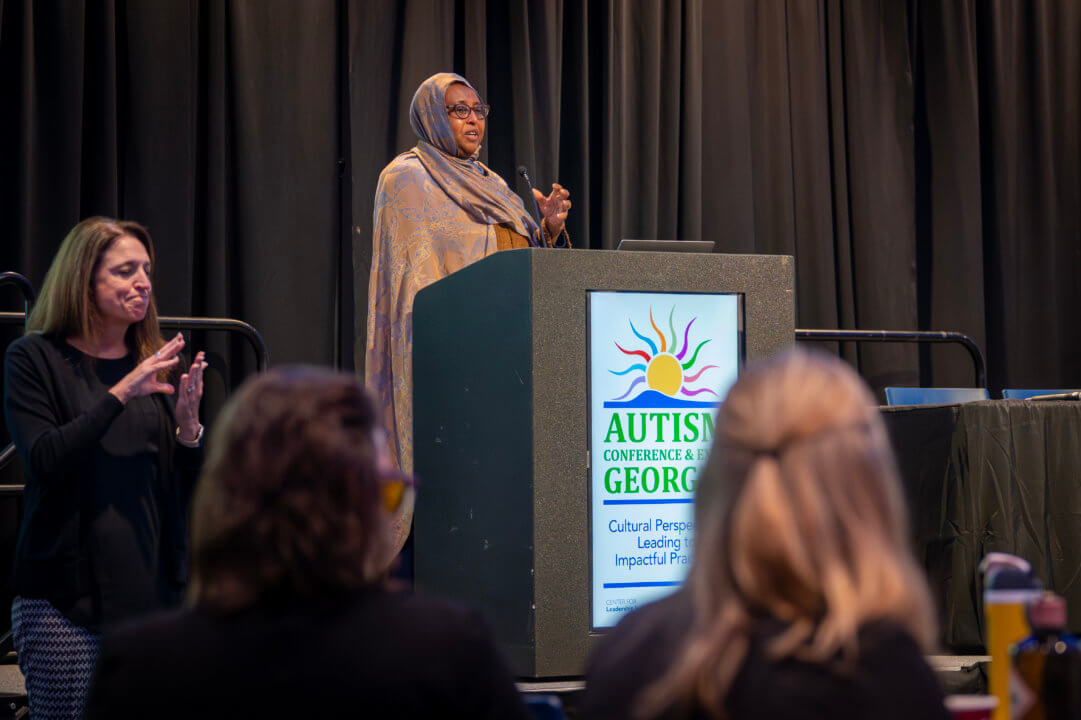 Woman with headwrap speaking at the podium, next to her is a female ASL interpreter