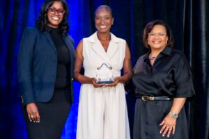 woman receiving award smiles on stage with two other women