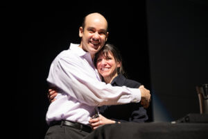 Man with big smile hugging woman with big smile on stage