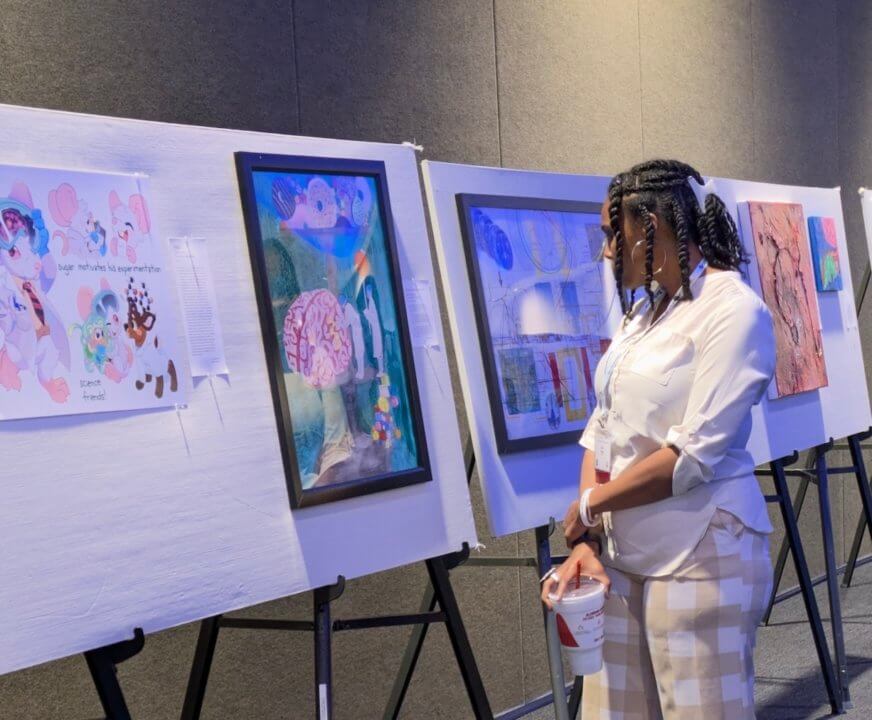 a woman stands and looks at mulitple paintings on easels