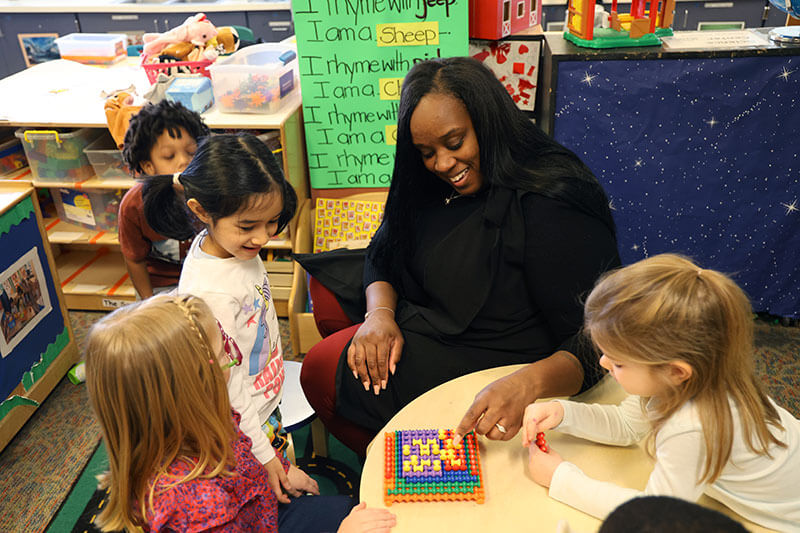 TaCara Rule-Ramsey works on a puzzle with three Pre-K students in the Child Development Center