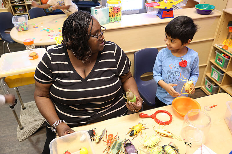Yolanda Maheia and one of her Pre-K students sit at a table holding plastic toy insects