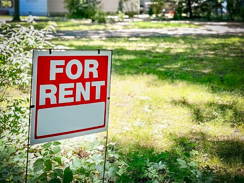 A red and white For Rent sign placed in a grassy residential yard, illustrating the growing trend of absentee owners managing properties across Atlanta neighborhoods.
