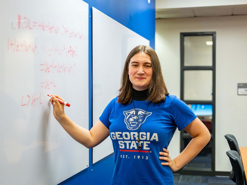 Ivanna Poliashenko writes mathematical equations on a whiteboard while wearing a Georgia State T-shirt.