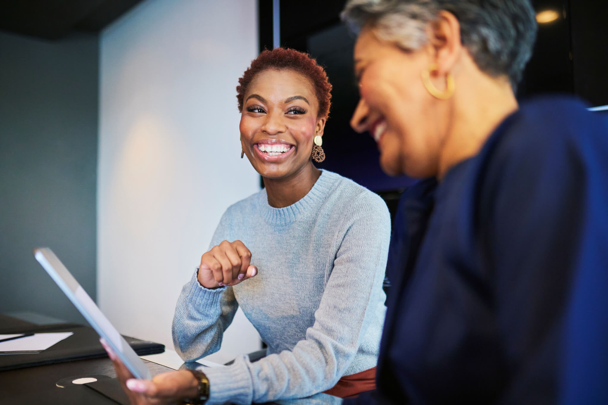 two professional women sitting at table in conference room, reviewing papers and smiling