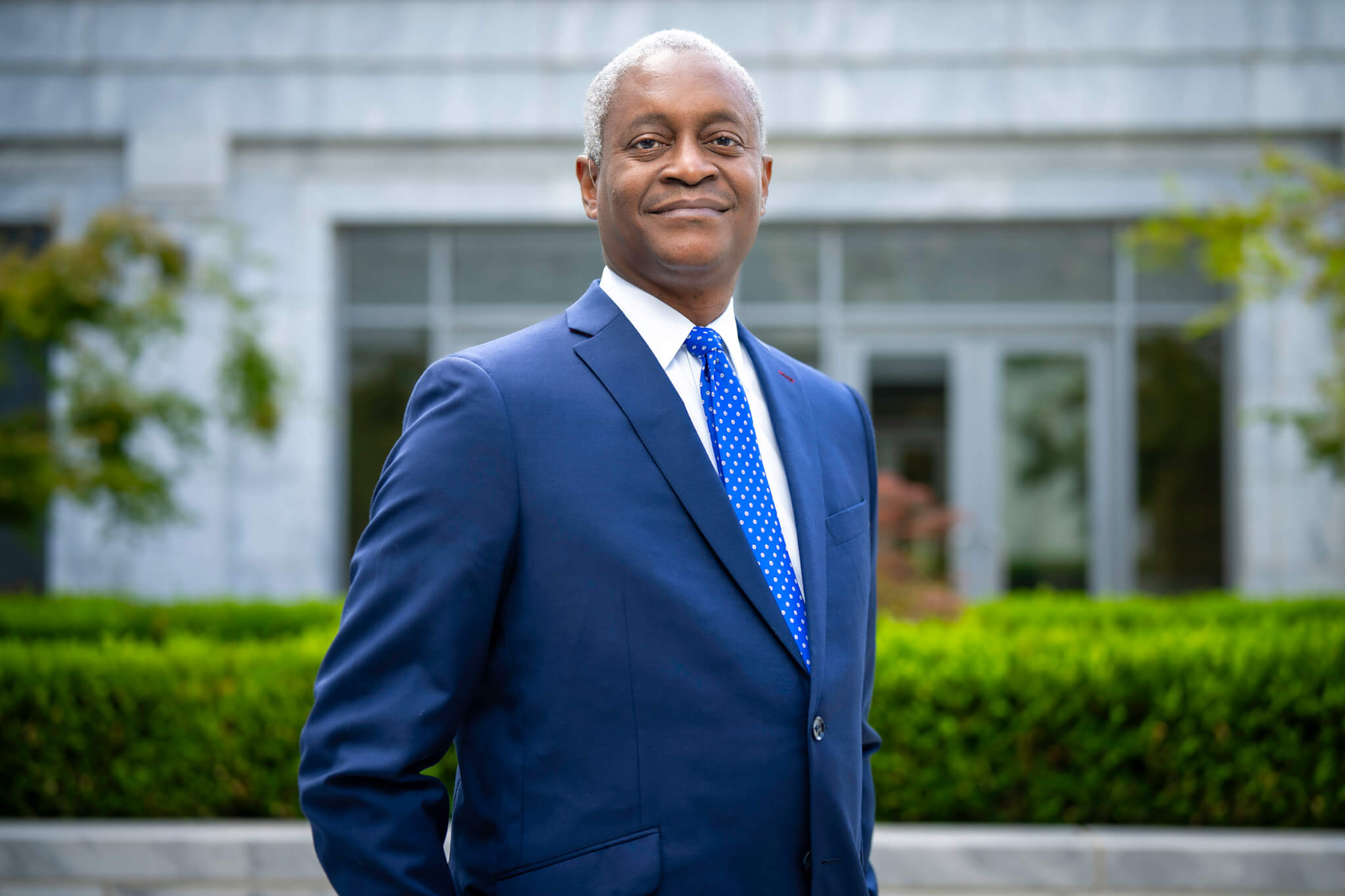 Raphael Bostic in blue blazer and light blue tie standing in front of the Atlanta Federal Reserve